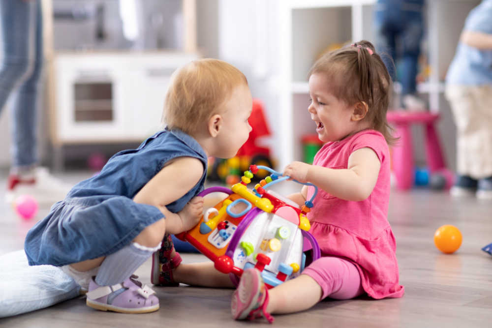 toddlers playing seem to be fighting over a plastic toy.
