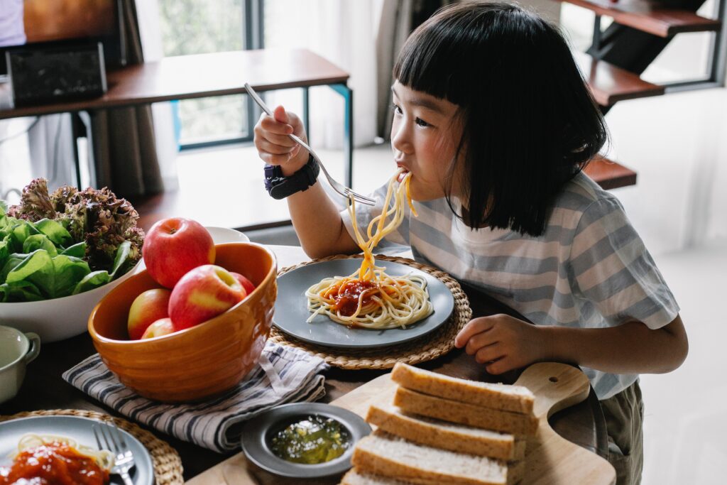 A child enjoying pasta with sauce, surrounded by other healthy foods.