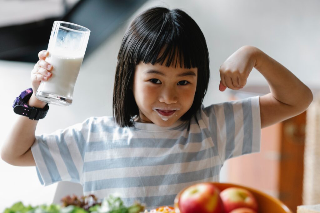 Happy child is smiling and showing their muscles after eating healthy foods and drinking milk.