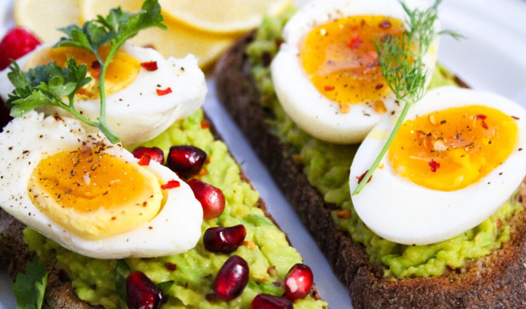 Hard-boiled eggs on top of avocado toast, sprinkled with pomegranate seeds.